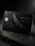 Black metal credit card engraved with a tall mountain landscape, Hebrew lettering, and the tagline Everything is in Heaven's Hands